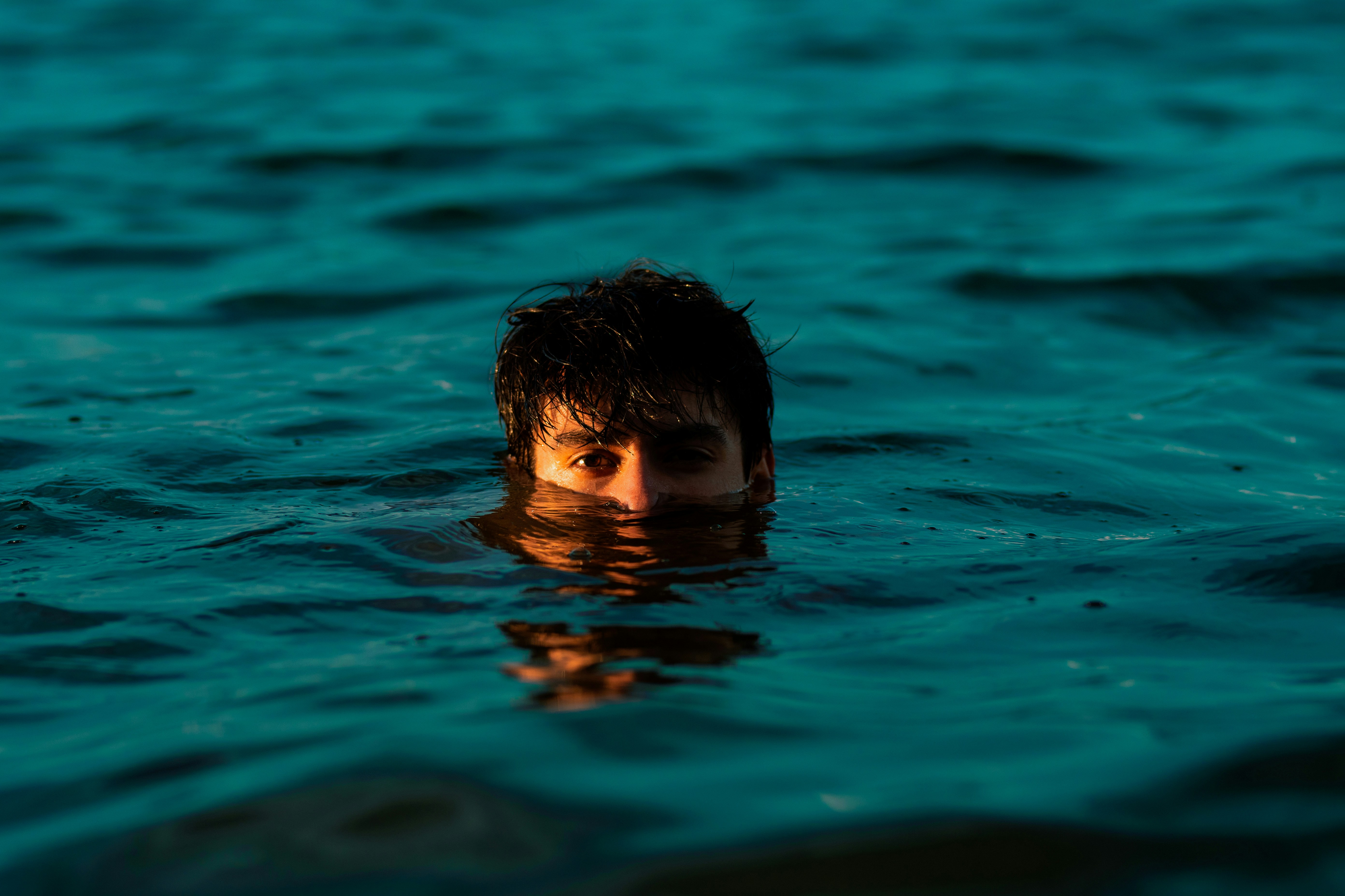 This scene depicts a person's head protruding from the water in what seems to be a beach setting. A young male’s head rise...